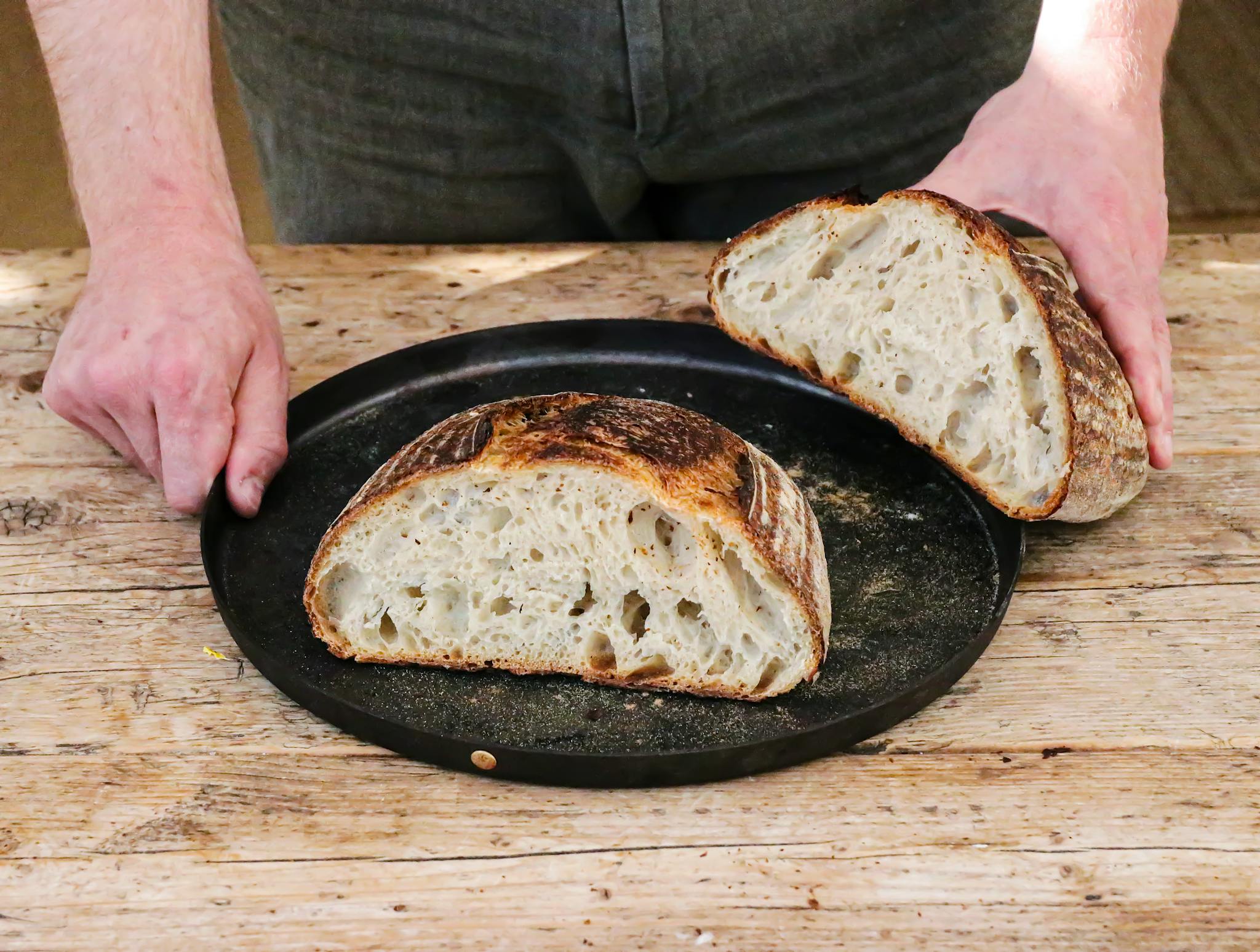 Artisan sourdough bread freshly sliced on a rustic wooden table, presented by a baker.