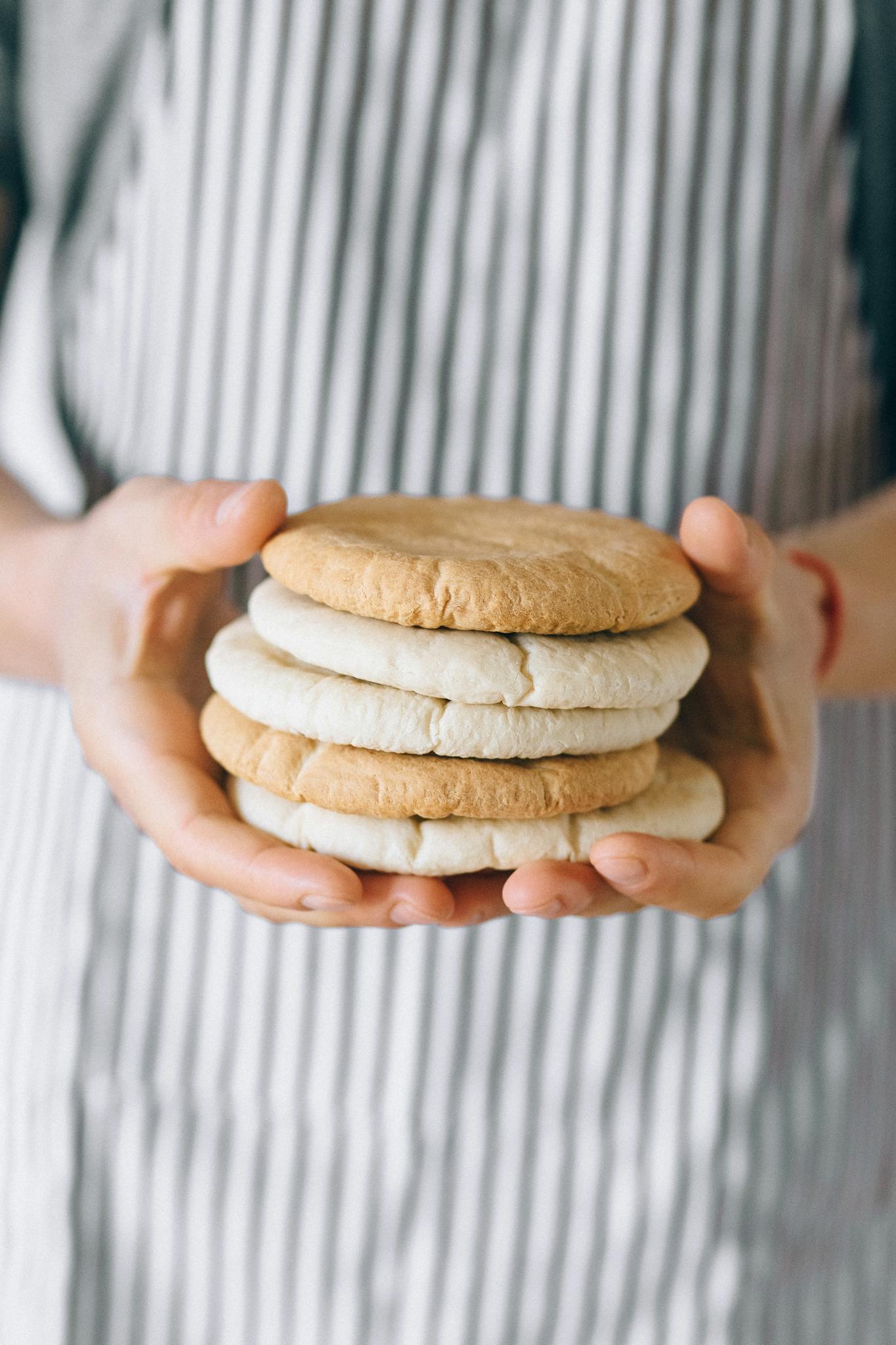 Close-up of hands holding a stack of freshly baked bread against a striped apron.