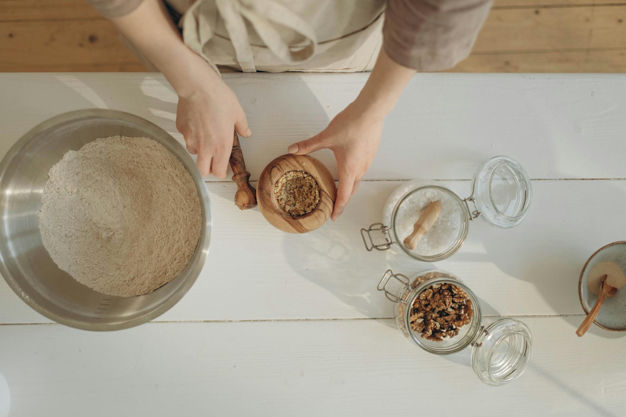 Hands preparing baking ingredients with nuts and flour on a white table.